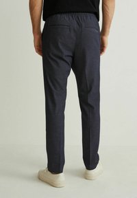 Granatowe spodnie z elastyczną talią, posiadające dwie tylne kieszenie. Noszone z jasnymi trampkami, przedstawione na neutralnym tle.