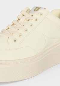 Κρεμ χρωματιστό χαμηλό sneaker με παχιά ραβδωτή σόλα, κορδόνια και σήμανση "Hugo" στη γλώσσα.