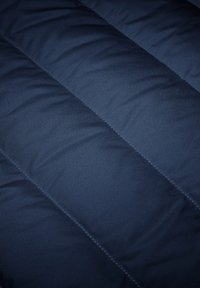 Navy blauwe gewatteerde stof met een gladde textuur en gestikte diagonale patronen, die een lichte, geïsoleerde uitstraling presenteert.