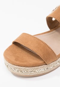Sandale ouverte en daim beige avec une large bride frontale, une semelle plateforme en jute tressé et une bande d'accent pailletée le long du bord de la semelle.