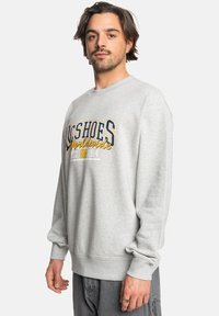 Sudadera gris hecha de material suave, con un bold logo en azul y amarillo en la parte delantera y puños y dobladillo acanalados para un ajuste relajado.