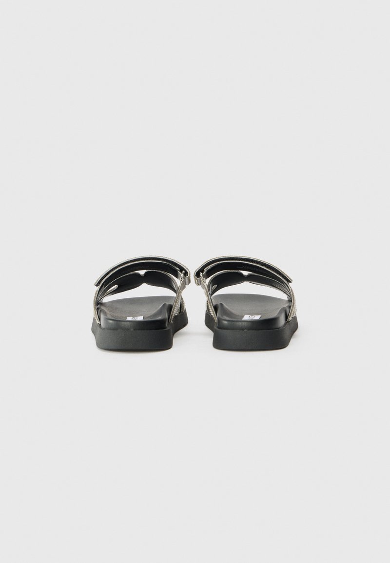Sandales noires avec deux sangles ajustables, une semelle plate et un semelle intérieure lisse et texturée. Vue arrière montrant le design et les détails des sangles.
