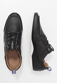 Black leather shoes with a smooth finish, rounded toe, and light-colored sole. Features include lace-up design and a blue-striped heel tab.