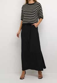 Gestreifter Strick-Crop-Top in Schwarz und Creme, kombiniert mit einem langen schwarzen Maxirock mit Taschen und einem seitlichen Schlitz.