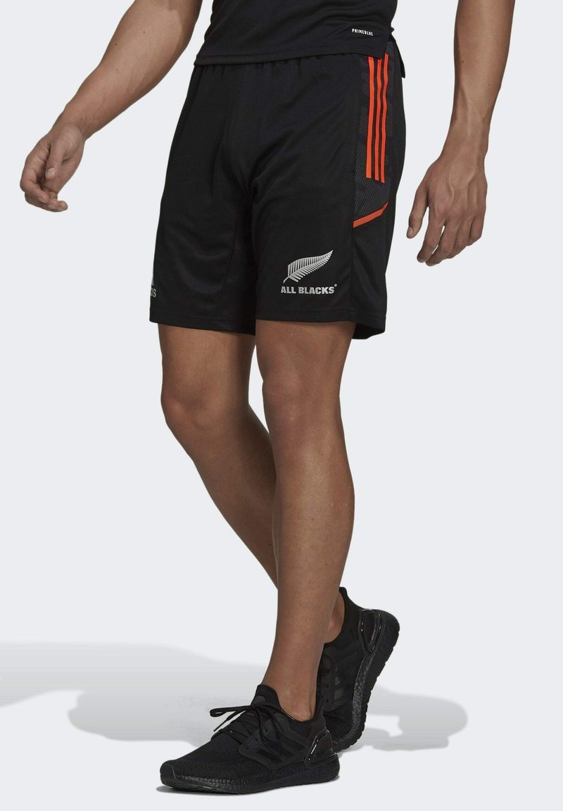 Svarta sportshorts med orange detaljer, meshmaterial, sidofickor och "ALL BLACKS"-logotyp tryckt på nedre vänstra sidan.