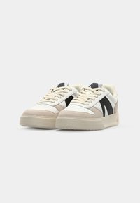 Sneakers z białą skórzaną cholewką, beżowymi zamszowymi akcentami, czarnymi panelami bocznymi, płaskimi kremowymi sznurówkami oraz teksturowaną gumową podeszwą.