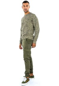 Maglione lavorato a maglia verde oliva con un motivo texture, abbinato a pantaloni cargo verde oliva con tasche laterali e polsini elasticizzati, completato da sneakers verdi.