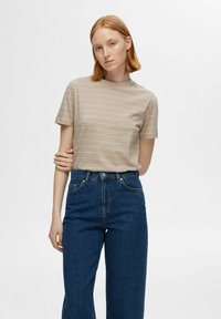 Camiseta de manga corta beige con rayas blancas horizontales, cuello redondo, combinada con jeans azules de tiro alto, con un corte holgado.