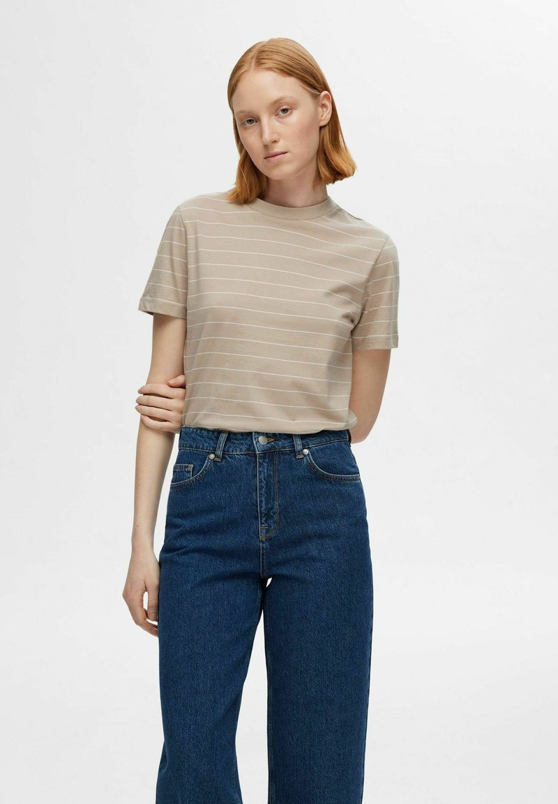 Camiseta de manga corta beige con rayas blancas horizontales, cuello redondo, combinada con jeans azules de tiro alto, con un corte holgado.