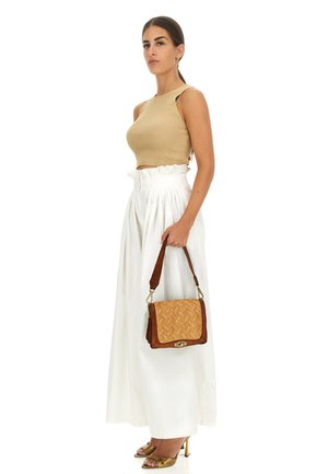 Borsa a tracolla intrecciata color tan con rifiniture marroni, caratterizzata da una forma strutturata e dettagli in oro. Indossata con un top beige e una gonna plissé bianca.
