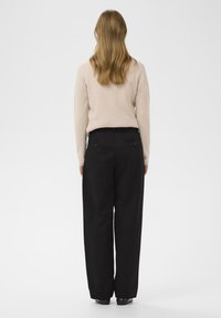 Schwarze weit geschnittene Hose mit hoher Taille, strukturierter beige gerippter Pullover und schwarze Schuhe. Schlichte Stoffe ohne sichtbare Muster.