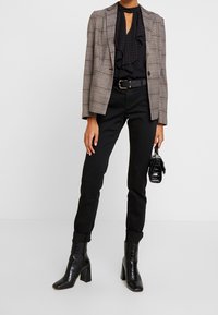 Kostkovaný sako s šedými a červenými liniemi, černá volánková blůza, černé kalhoty, černé boty na podpatku a malá černá kabelka.