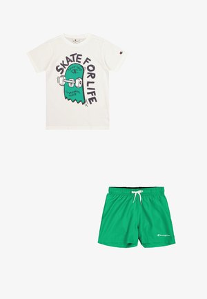 T-shirt bianca con grafica di uno skateboard verde e nero e la scritta "SKATE FOR LIFE." Costume da bagno verde con vita elastica e coulisse.