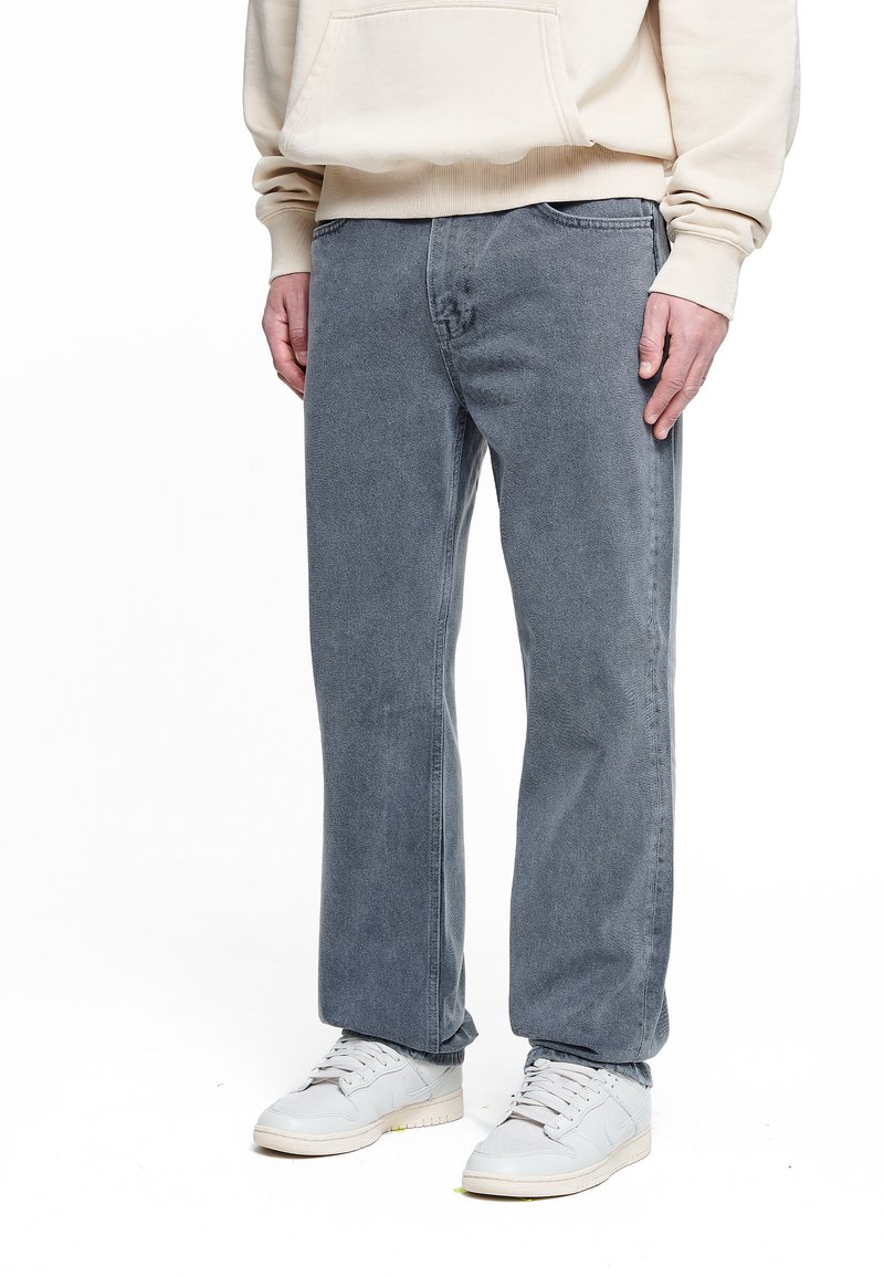 Grå denim jeans med lige snit og subtil tekstur, kombineret med lyse sneakers og en beige hoodie med kengurulomme.