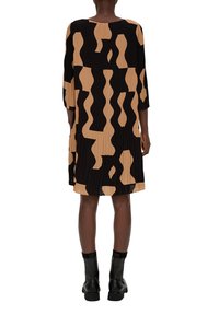 Zwarte geplooide jurk met abstract beige patroon, driekwart mouwen, ronde halslijn en een losse pasvorm, gecombineerd met zwarte enkellaarsjes.