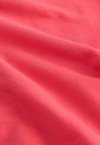 Tela de algodón coral con una textura suave, presenta estrías sutiles y un brillo uniforme, doblada en ondas suaves.