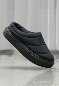 Svart quiltet slip-on sko med polstret krage og teksturert yttersåle. Har et logo-patch på siden og en avrundet tådesign.