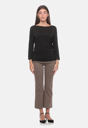 Donna in piedi di fronte indossa una maglia nera a maniche lunghe, pantaloni marroni corti e tacchi neri con cinturino alla caviglia su uno sfondo semplice.
