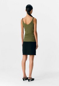 Top de tirantes acanalado color verde oliva con un diseño en V en la parte de atrás, combinado con una mini falda negra. La modelo lleva unos tacones tipo slingback negros; diseño limpio y minimalista.