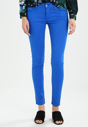 Jasnoniebieskie obcisłe dżinsy wykonane z bawełny, z dopasowanym krojem, przednimi kieszeniami i zapięciem na guzik, w połączeniu z czarnym obuwiem z odkrytymi palcami.