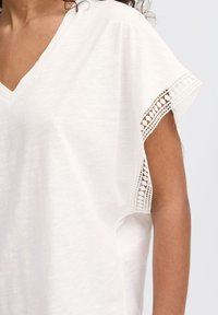 White V-neck top with lace trim on sleeves, made from lightweight fabric, featuring loose fit and soft texture.