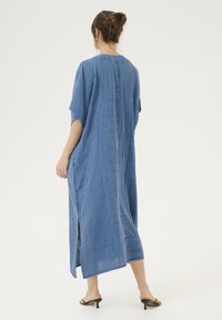 Zila, līdz ceļiem gara kleita, izgatavota no teksturēta, viegla auduma. Izvērsumi ir īsas piedurknes, sānu atveres un taisna griezuma ar aizmugures šuves detaļu.