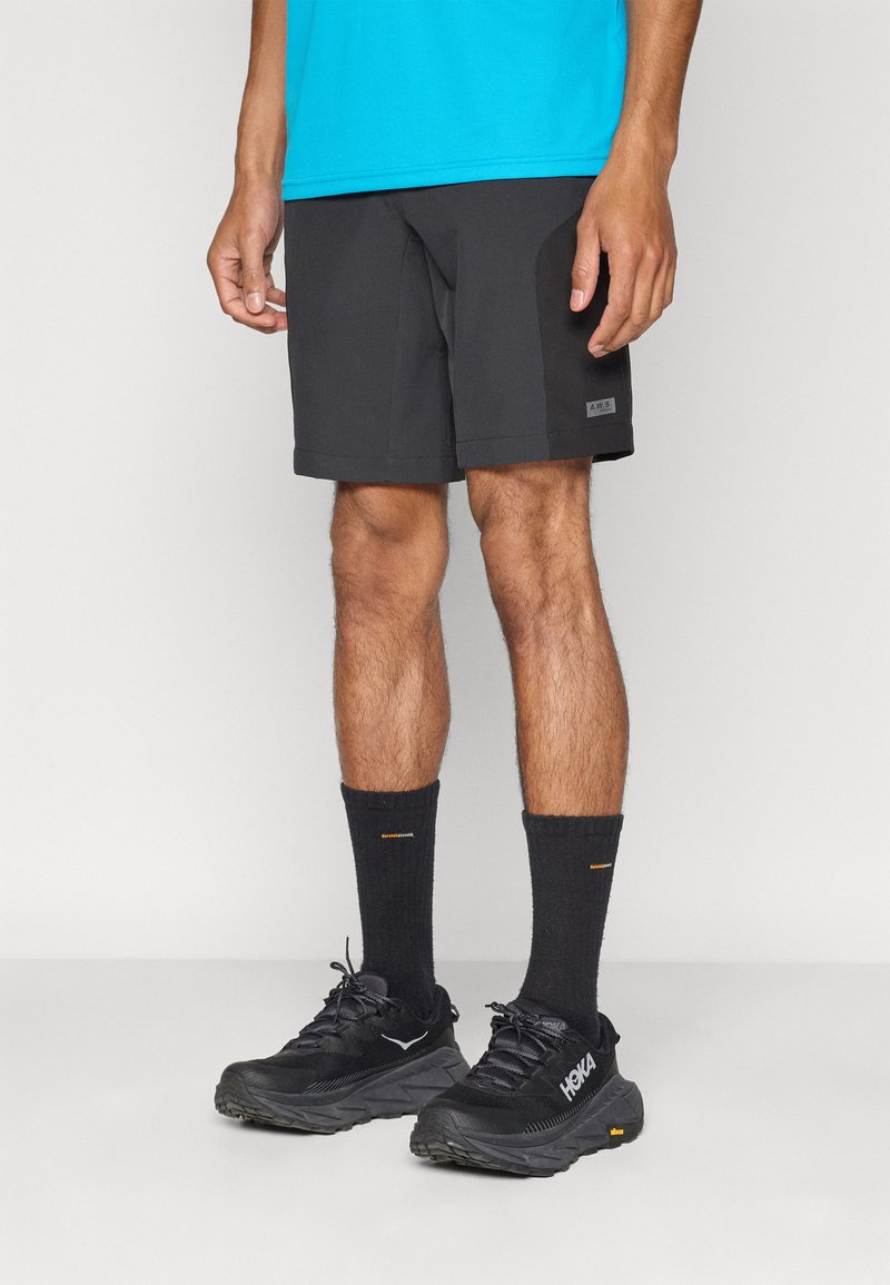 Schwarze Sportshorts mit glatter Textur und Logopatch, kombiniert mit schwarzen Socken und schwarzen Laufschuhen mit einer geschichteten Sohle.