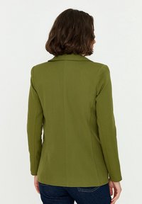 Oliwkowa marynarka wykonana z gładkiej tkaniny, z kołnierzem z wycięciem, długimi rękawami i dopasowanym krojem. Widok z tyłu ukazuje czyste linie.