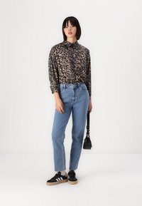 Luipaardprint, langemouw shirt in bruin en zwart, gecombineerd met high-waisted, lichtblauwe denim jeans. Zwarte sneakers met witte accenten.