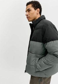 Pufferjacka i svart och dämpad grön färg. Har dragkedja framtill, hög krage, horisontellt quiltat mönster och sidofickor. Texturerat tyg.