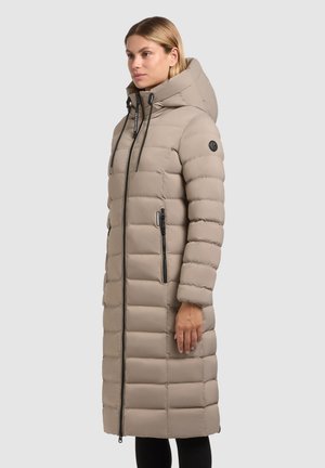 Garšs bežs pūkains mētelis ar kapuci, ar priekšējo rāvējslēdzēju, horizontālu quilted rakstu un melniem akcentiem. Sānos ir rokassomi.