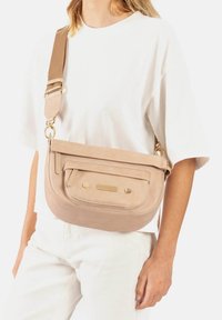 Beige lederen schoudertas met een voorvak, gouden hardware accenten, verstelbare schouderband en ingewikkelde stiksel-details.