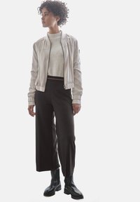 Giubbotto bomber grigio chiaro con polsini a costine, maglione crema, pantaloni neri a gamba larga e stivali neri alla caviglia. Design semplice e moderno.