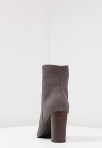 Botín de ante gris con parte superior redondeada y tacón de madera grueso, que presenta líneas limpias y una textura suave.