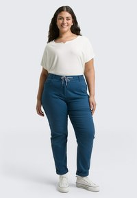 Lichtgewicht wit T-shirt met een brede halslijn, gecombineerd met losvallende blauwe broek met een trekkoord en opgerolde mouwen.