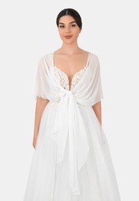 White dress featuring a sheer, draped overlay tied at the waist, with lace detailing on the bodice and a flowing, textured skirt.