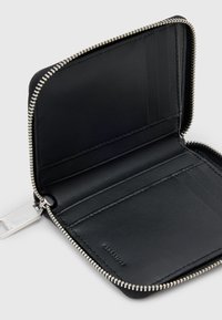 Portafoglio in pelle nera con chiusura a zip. L'interno presenta slot per carte e una texture liscia. È visibile hardware argentato attorno alla cerniera.