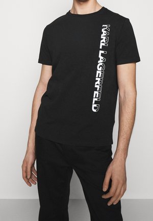 T-shirt en coton noir avec un imprimé logo vertical blanc sur le côté gauche. Col rond et manches courtes, avec une coupe décontractée.