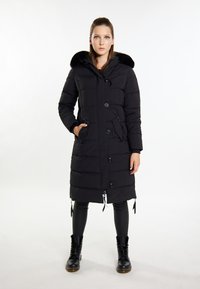 Sort polstret jakke med en kunstpels hætte, frontknapper, sidelommer, justerbar talje og snoretræk i bunden. Bæres over sorte leggings og støvler.