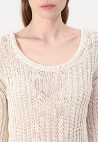 Maglione lavorato a maglia beige chiaro con scollo ampio, caratterizzato da un motivo testurizzato e una vestibilità morbida, realizzato in un materiale morbido e traspirante.
