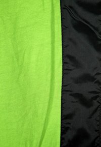 Prim-plan cu țesătură tricotată neon verde lângă țesătură sintetică neagră netedă, cu o linie de cusătură vizibilă între ele.