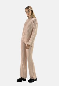 Conjunto de ropa cómoda de punto acanalado en rosa suave, que incluye una parte superior de corte relajado con mangas largas y pantalones de pierna ancha a juego. Zapatos de plataforma negros.