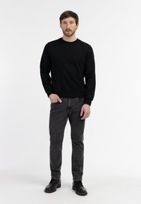 Czarny sweter z okrągłym dekoltem i ściągaczami na rękawach, w połączeniu z ciemnoszarymi dżinsami slim-fit i czarnymi skórzanymi botkami, stojący na białym tle.