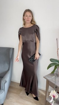 Vestido de noite de cetim castanho-escuro com mangas curtas pregueadas, corpete ajustado e bainha ampla, combinado com uma carteira preta e sapatos de salto pretos de bico.