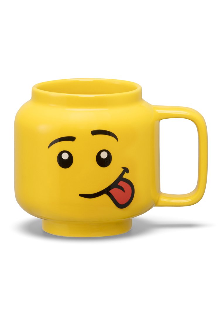 Tazza in ceramica gialla a forma di faccia sorridente, con occhi, lingua di fuori e un manico robusto. Corpo rotondo con finitura liscia.