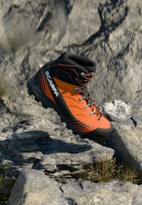 Stivale da hiking arancione con accenti neri, suola in gomma e occhielli in metallo. Presenta un materiale testurizzato e un sistema di allacciatura per una vestibilità sicura.