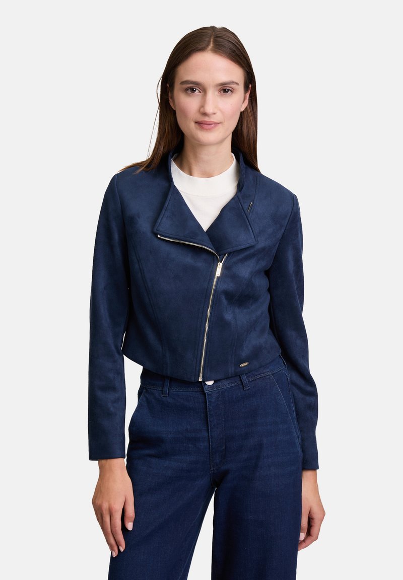 Navyblaue, künstliche Wildleder-Cropped-Jacke mit großem Revers, asymmetrischem Reißverschluss und langen Ärmeln, kombiniert mit dunklen Denim-Hosen.