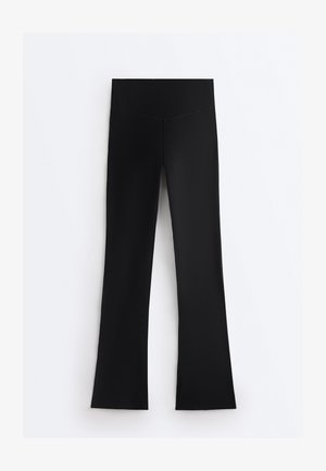 Črne visokega pasu legice s širokim pasom, z ravnim krojem nogavic, postavljene na ravno površino na belem ozadju.