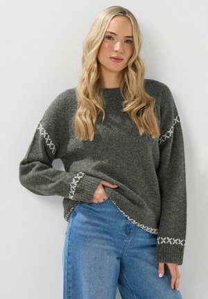 Maglione grigio a maglia con una vestibilità comoda, caratterizzato da accenti ricamati bianchi sulle maniche e sull'orlo. Abbinato a jeans in denim blu.