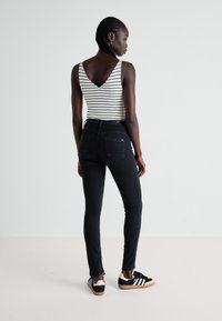 Jeans negros ajustados combinados con una blusa de tirantes a rayas. Los jeans tienen un diseño clásico con dos bolsillos traseros.